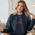 
I'm OK! (Drowning Character) Navy crewneck sweatshirt with embroidered "I'm ok!" humorous design featuring a small character with raised hands sinking in water, stitched in cream thread, displayed on a female model seated on a white couch.